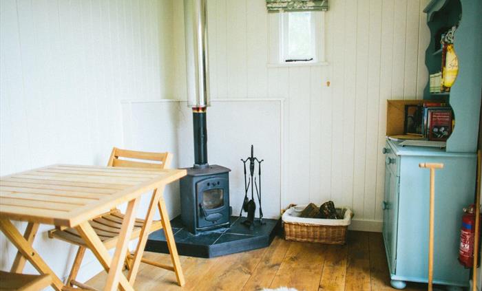 The inside of the shepherd's hut with sheepskin rug on the oak floor, blue welsh dresser, wood-burning stove with a basket of logs and a small oak tab